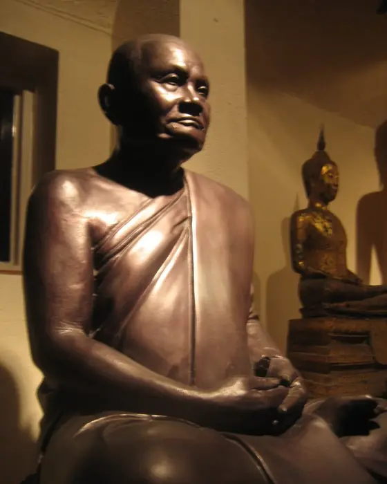 A dark bronze-coloured statue of a seated monk with a calm expression.