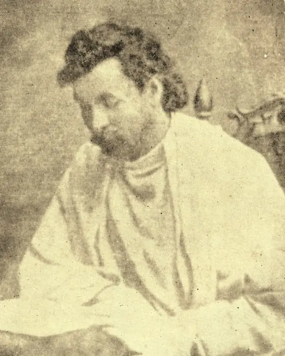 A sepia photograph of a young man with curly hair in a pale robe, head bowed.