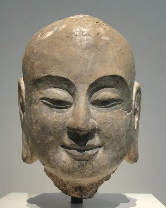 A limestone head of a young smiling monk with a shaven head.