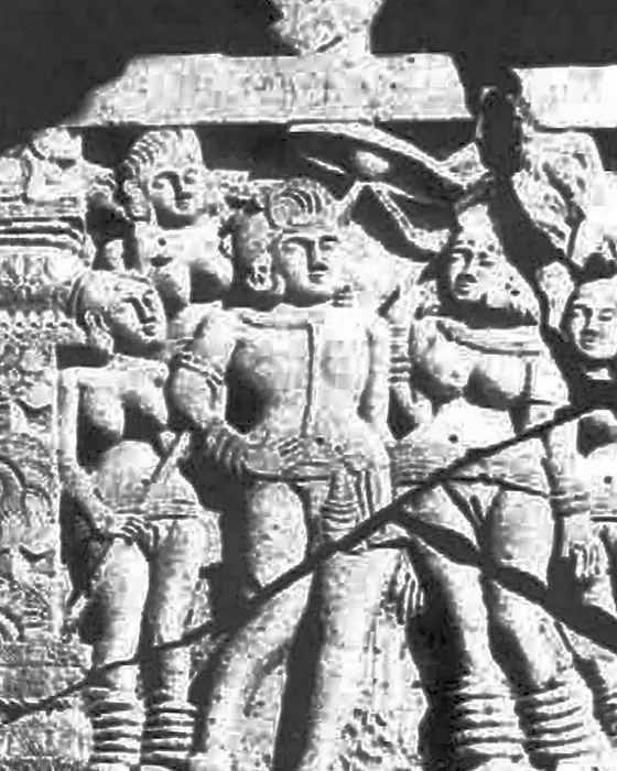 A black-and-white photograph of a worn stone relief of a king standing with women attendants.