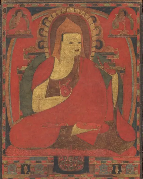 A painting of a seated monk in a red robe and pointed pandit's hat, on a red ground.