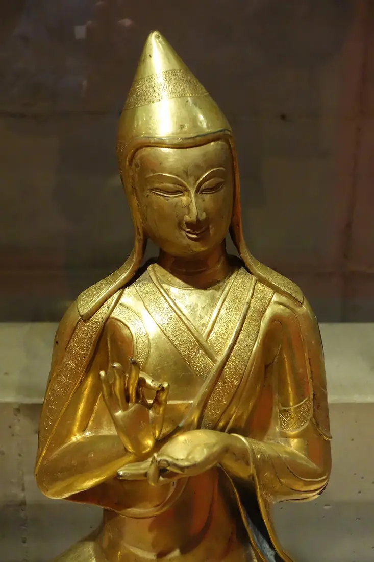 A gilded bronze figure of a monk in a tall pointed hat.