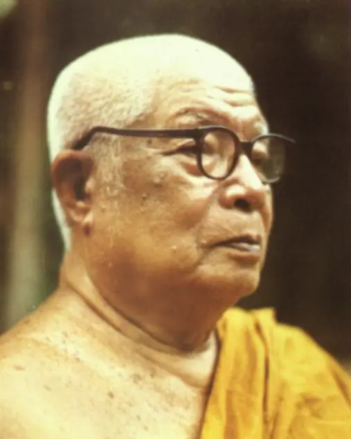 A colour photograph of an elderly monk with glasses and a yellow robe.