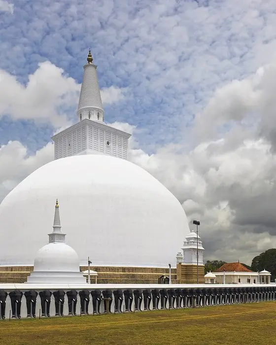 A vast white dome-shaped stupa under a cloudy sky.