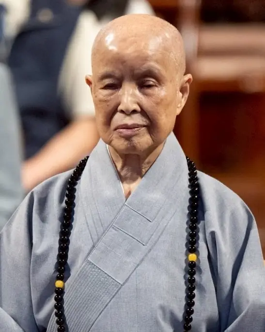 A colour photograph of an elderly nun in grey robes with long prayer beads.