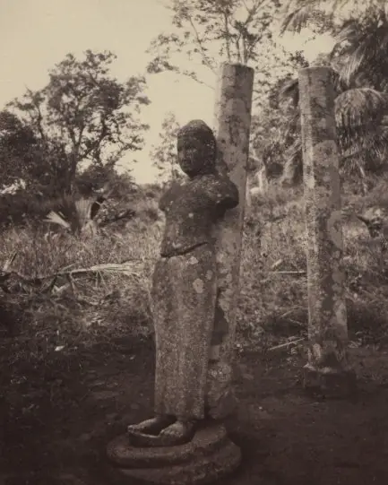 A faded photograph of a weathered standing stone figure among trees.