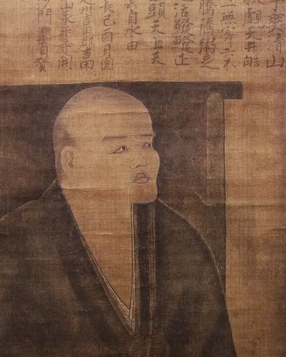 A painting of a monk seated in dark robes on a chair, gazing up.