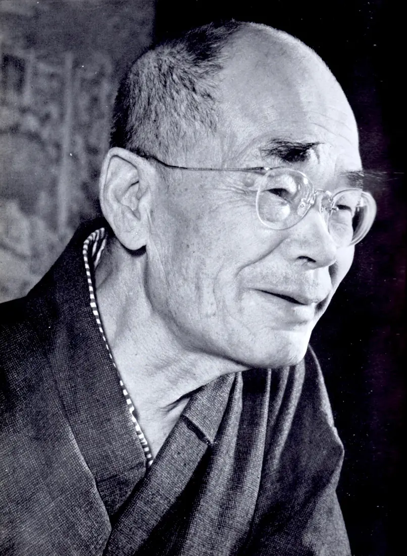 A black-and-white portrait of an old man in glasses looking down.