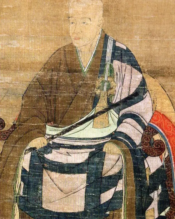 A painting of an elderly monk seated in a chair in patterned robes, holding a staff.