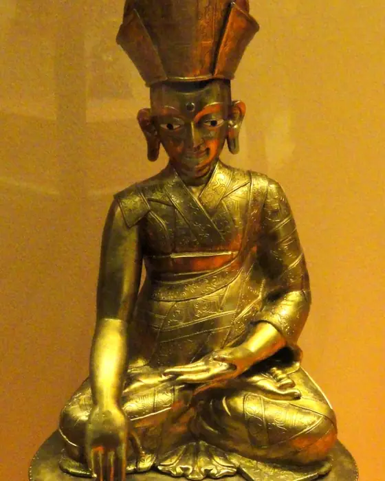 A gilded seated figure of a teacher in a tall hat, on a lotus base.