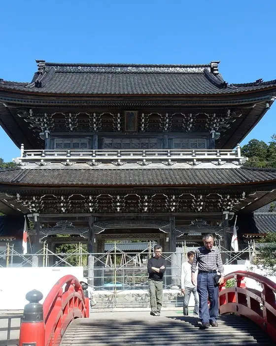 A large two-storey wooden temple gate beyond a red bridge.