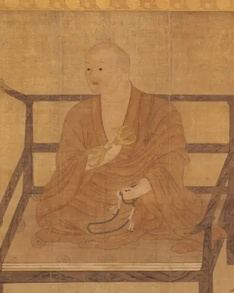 A hanging scroll of a monk seated in a wooden chair holding a ritual implement.