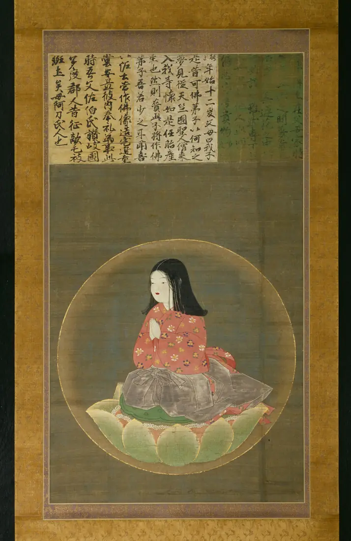 A hanging scroll of a child in red robes seated on a lotus within a circle.