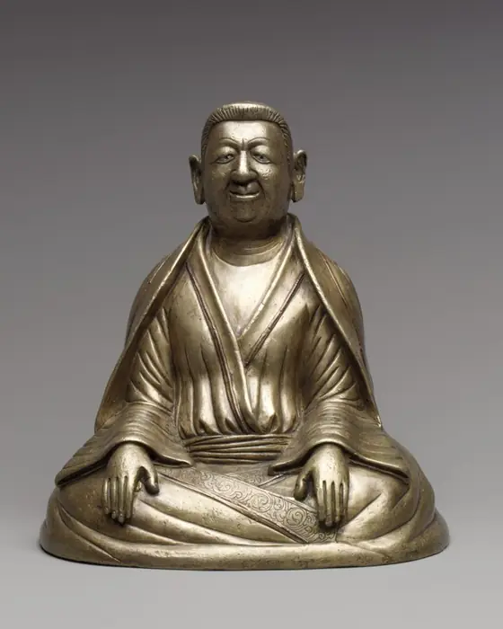 A bronze seated figure of a heavy-set man with a round face and hands resting on his knees.