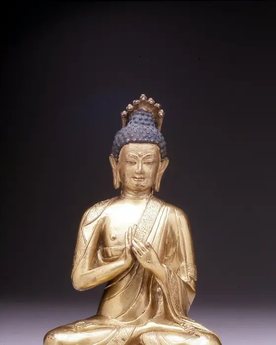 A gilded seated figure of a teacher with a halo of serpent hoods, his hands raised before his chest.