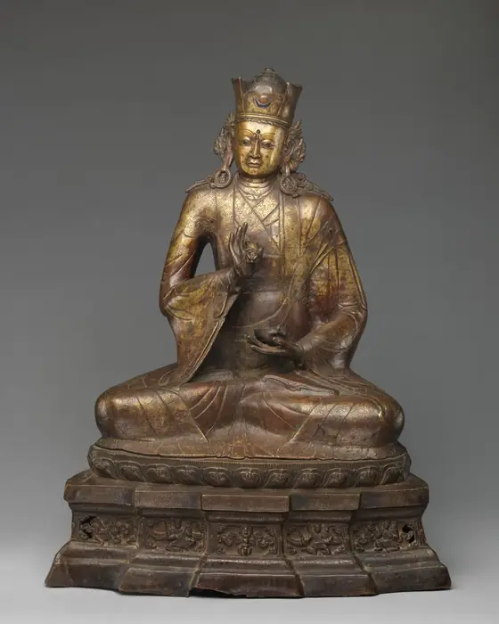 A seated metal figure in a crown and robes, on a tall base.