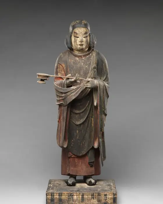 A wooden statue of a young man with long hair, standing and holding a censer.