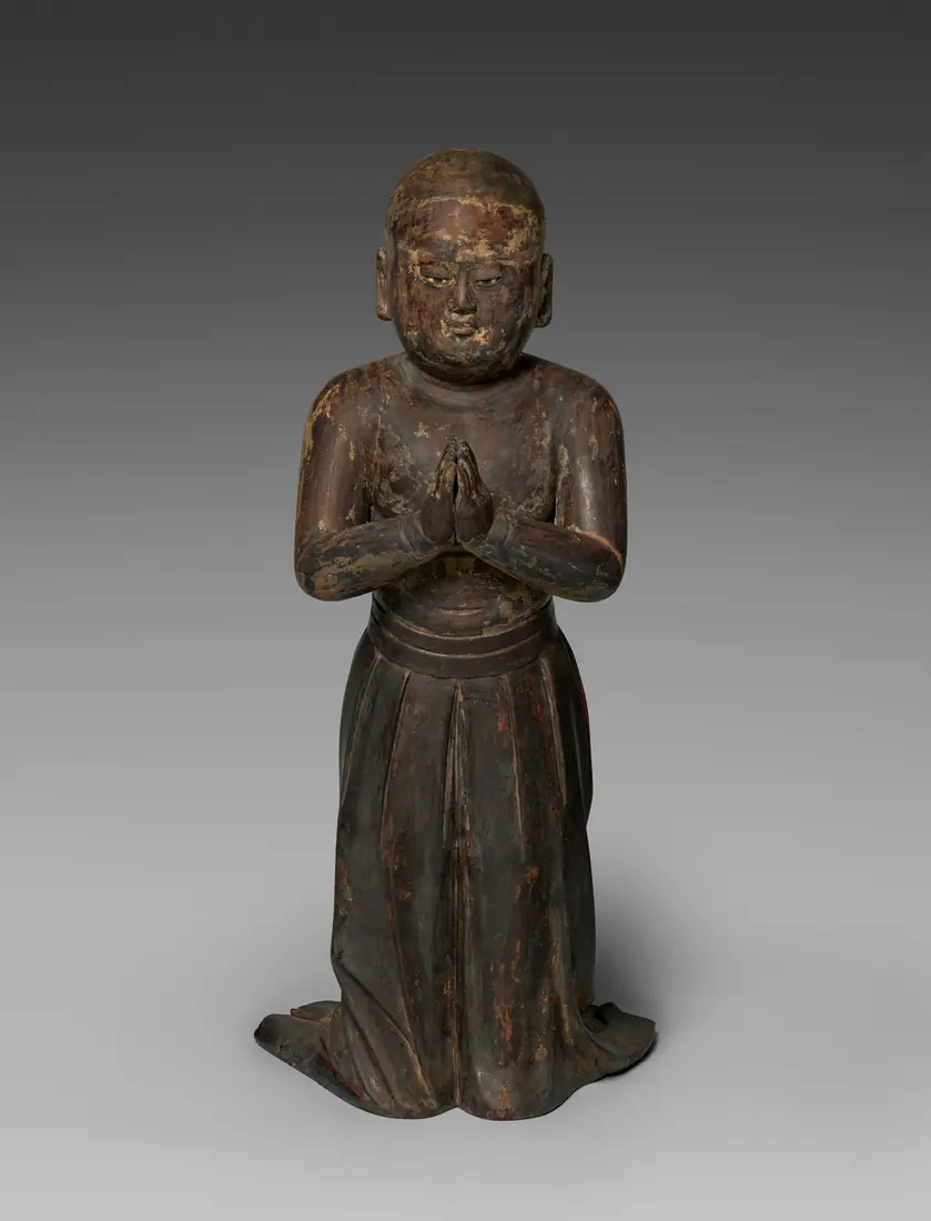 A wooden statue of a small child with hands joined in prayer.