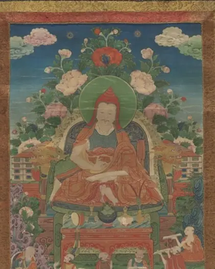 A mounted Tibetan painting of an abbot in a red hat seated among flowers, framed in dark brocade.