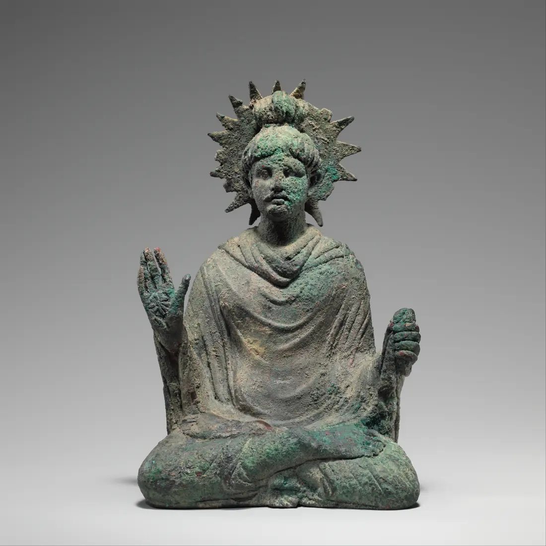 A small bronze-coloured seated Buddha with a radiating halo, his hand raised.