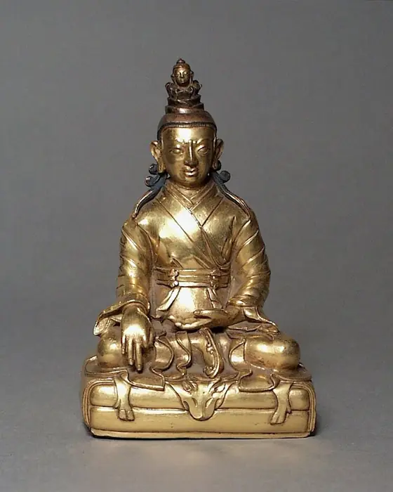 A gilded brass seated king with a tall turban topped by a small head.