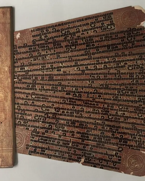 Gilded palm-leaf pages covered in bold dark script, with a lacquered cover.