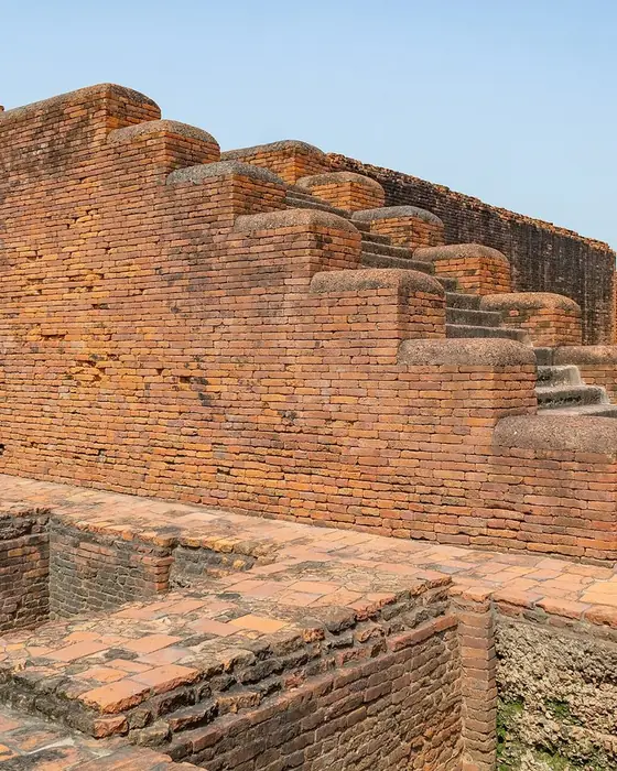 Red brick ruins of monastic cells and stairs under a pale sky.