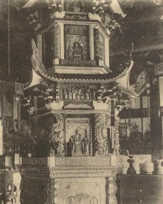 An old photograph of an ornate stone pagoda inside a temple hall.