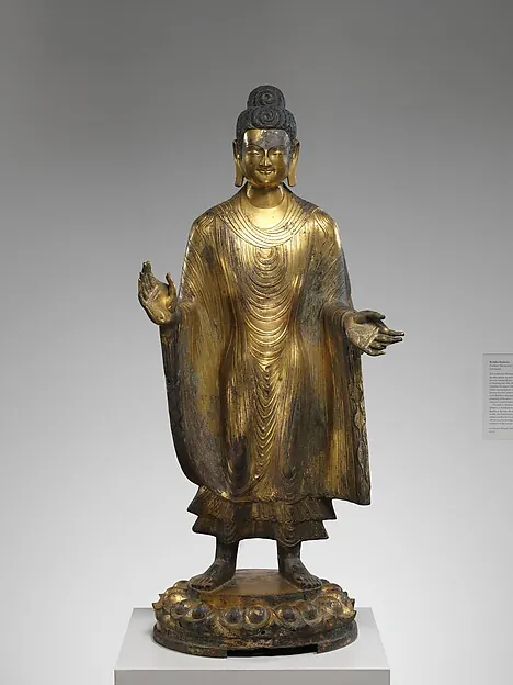 A standing gilt bronze Buddha with one hand raised, on a lotus base.