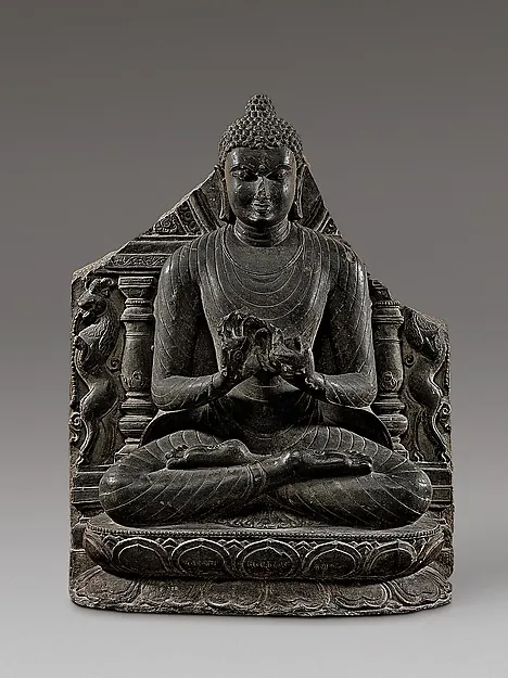 A black stone Buddha seated cross-legged, hands in the teaching gesture, set within a carved throne back.
