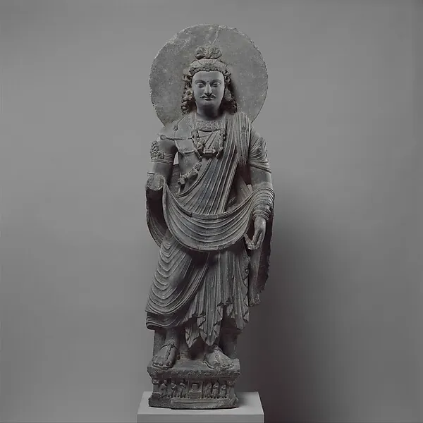 A standing grey stone figure of a bodhisattva in draped robes and jewellery, with a halo.